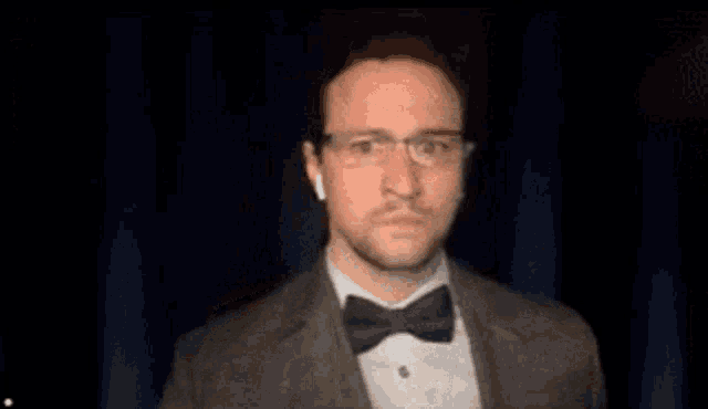 a man in a suit and bow tie is wearing headphones and glasses .