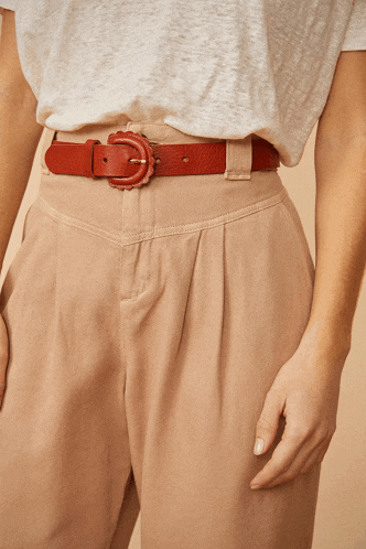 a woman wearing a white shirt and tan pants has a red belt around her waist