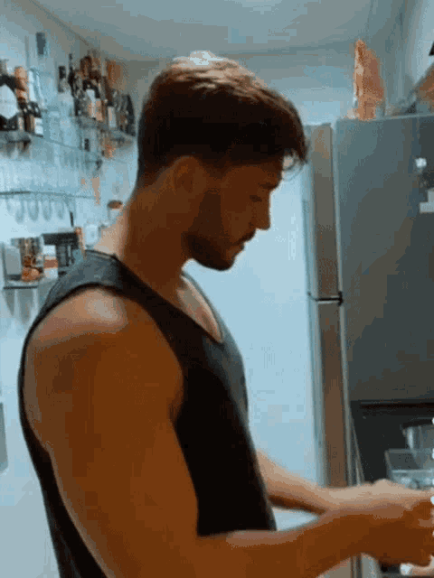 a man in a black tank top is cooking in a kitchen