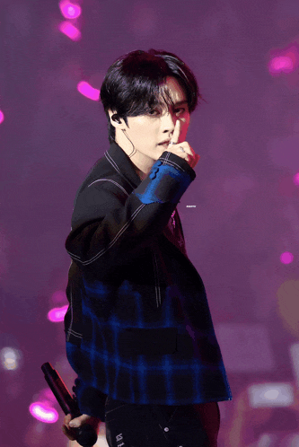 a young man in a plaid jacket is holding a microphone in his hand