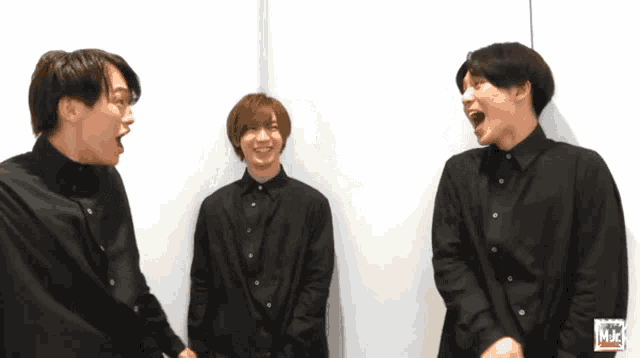 three men in black shirts are standing next to each other and one of them is laughing while the other two are laughing