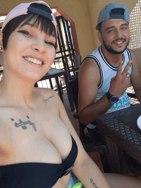 a man and a woman are posing for a picture and the woman has a tattoo on her shoulder that says " jesus "