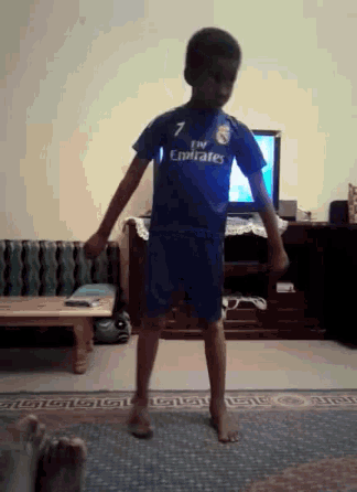 a young boy wearing a fly emirates shirt is dancing