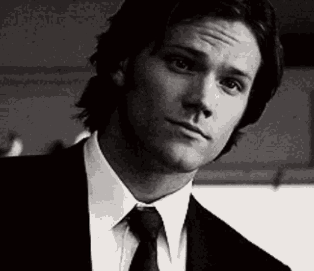 a man in a suit and tie looks at the camera with a serious look on his face