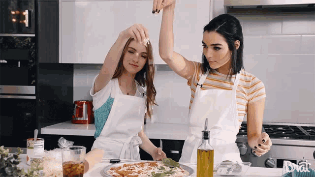 two women in white aprons are preparing a pizza in a kitchen that says brat on the stove