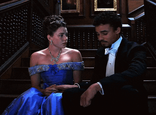 a woman in a blue dress sits next to a man in a tuxedo on the stairs