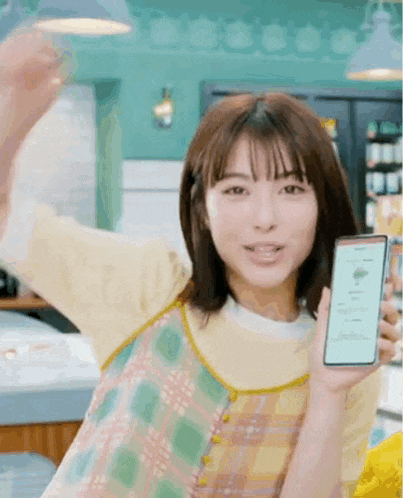 a woman in a plaid dress is holding a cell phone in her hand in a store .