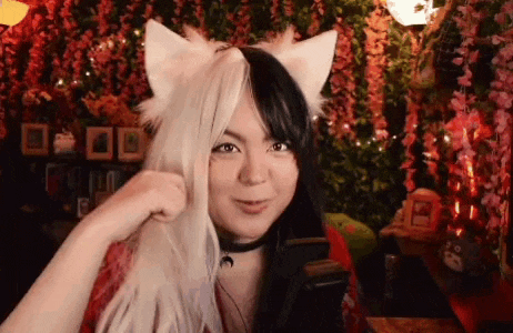 a woman wearing a cat ear headband and headphones is standing in front of a wall of flowers .