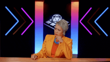 a woman in an orange suit is sitting at a table in front of a colorful background .