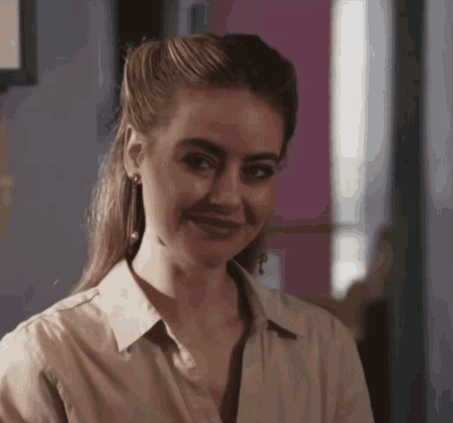 a woman wearing earrings and a tan shirt smiles at the camera