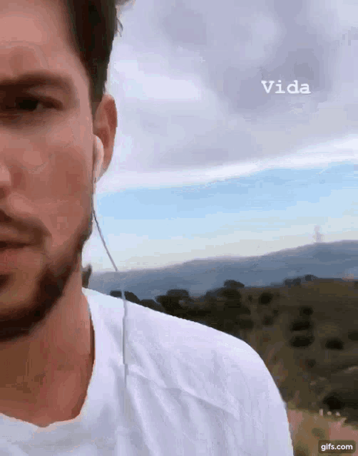 a man with a beard wearing ear buds and a white shirt with the word vida written above him