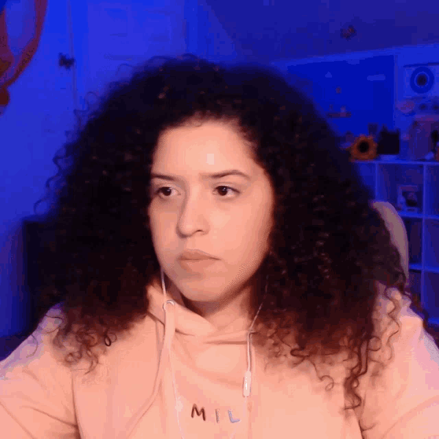 a woman with curly hair wearing a pink mil sweatshirt