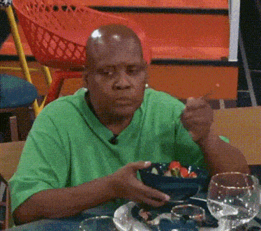 a man in a green shirt is eating a salad with a fork and knife .