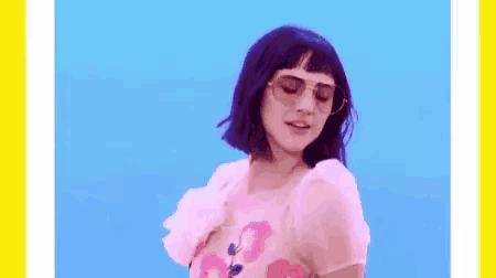 a woman wearing sunglasses and a pink shirt is dancing against a blue background .
