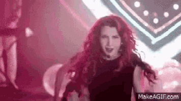 a woman with red hair is dancing on a stage in front of a pink light .