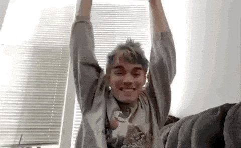 a young man is sitting on a bed with his arms in the air and smiling .