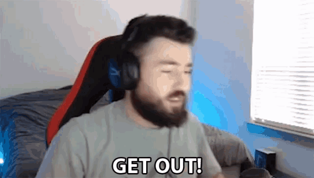 a man with a beard wearing headphones is sitting in a chair and saying `` get out '' .