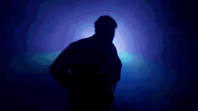a silhouette of a person in a dark room with blue lights behind them