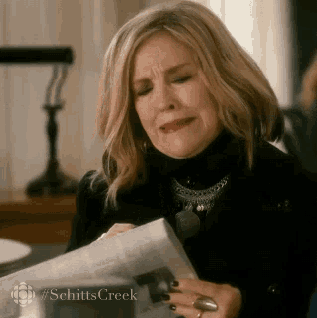 a woman is crying while reading a newspaper from schitt 's creek .