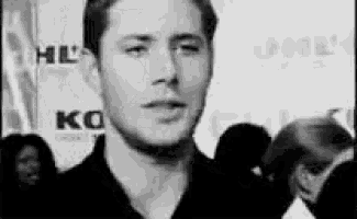 a man in a black shirt is standing in front of a crowd and making a funny face .