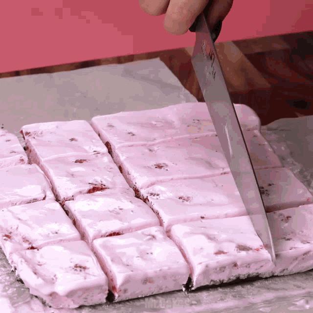 a person is cutting a piece of pink marshmallow