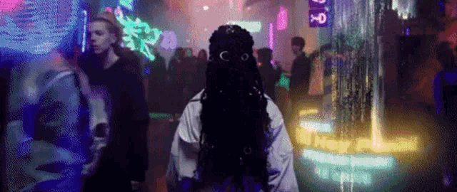 a woman with dreadlocks is standing in a crowded room with neon lights .