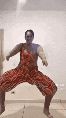 a woman in a red dress is dancing in a room with her legs crossed .