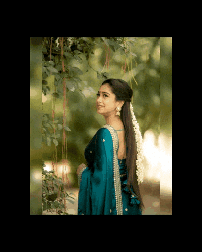 a woman wearing a blue saree is standing in front of a tree