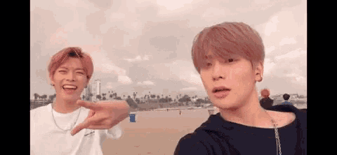 two young men are standing on a beach taking a selfie .