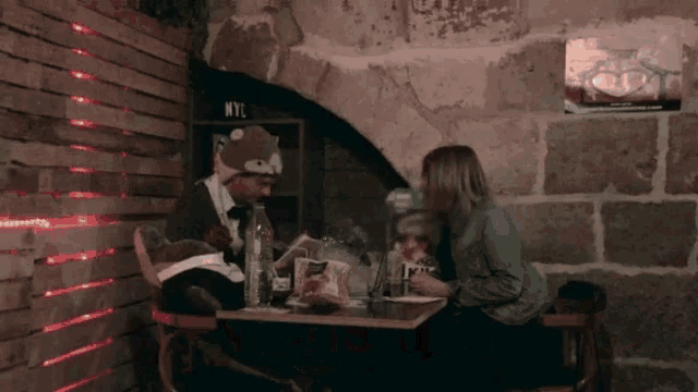 a man and a woman sit at a table in front of a wall with nyc written on it