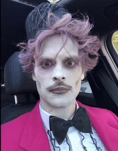 a man with purple hair and a mustache is wearing a pink suit and bow tie
