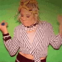 a woman wearing a mask and a striped jacket is dancing on a green screen .