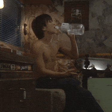 a shirtless man drinking water from a bottle with a sticker on the side that says kashi