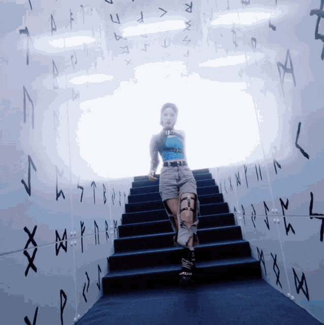 a woman walking up a set of stairs in a room with runes on the walls
