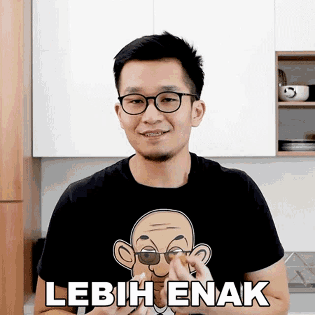 a man wearing glasses and a black t-shirt says lebih enak