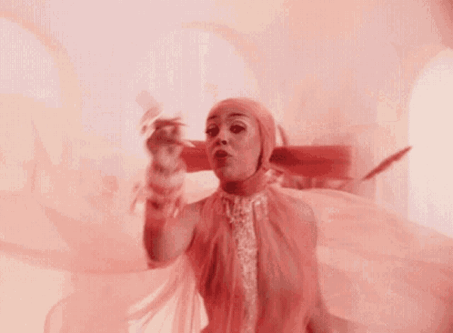 a woman in a pink dress is dancing in front of a pink wall