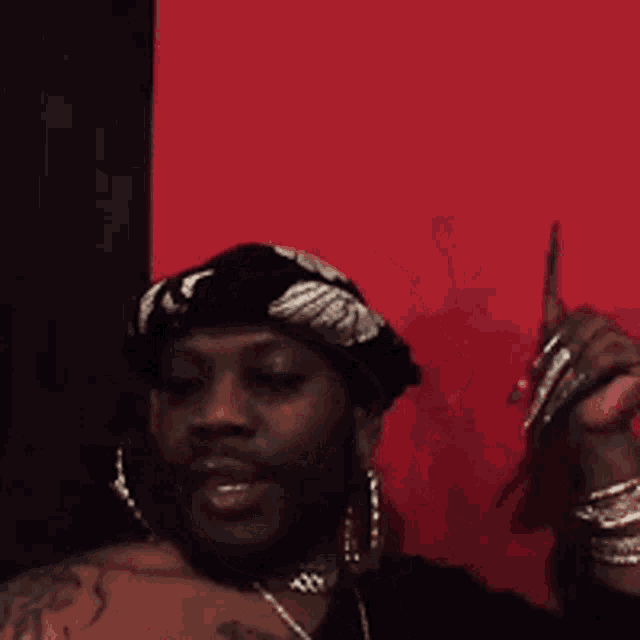 a man wearing a black hat and earrings is dancing in front of a red wall