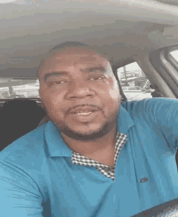 a man in a blue shirt is driving a car and making a funny face
