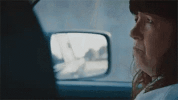 a woman is sitting in the back seat of a car looking at the side mirror .