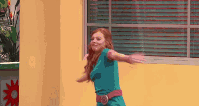 a girl in a blue shirt and pink belt is dancing in front of a window .