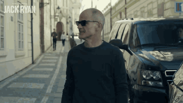 a man wearing sunglasses walks down a street with the name jack ryan on the bottom right