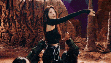 a woman in a black top is dancing in front of a rock formation