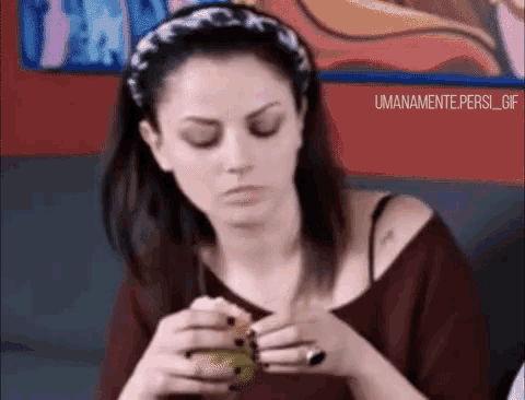 a woman wearing a headband and a ring is sitting on a couch eating a sandwich .