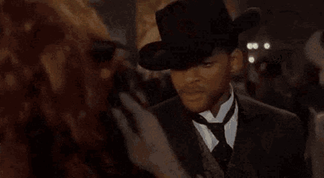 a woman in a choker is talking to a man in a suit and hat .