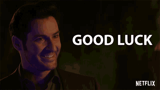 a man smiles in front of a sign that says " good luck "
