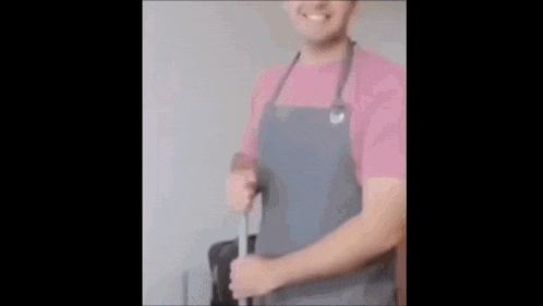 a man in an apron is cleaning a microwave with a sponge and smiling .