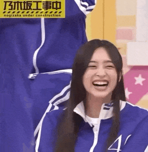 a woman in a blue jacket is smiling and laughing while sitting on a chair .