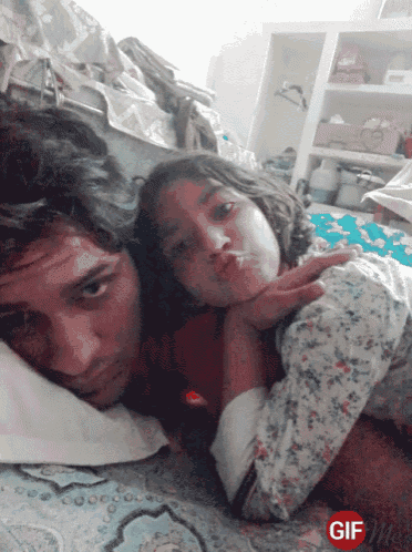 a man and a little girl are laying on a bed with a gif on the bottom
