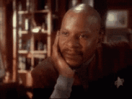 a man in a suit and tie is sitting in a room with his hand on his face .