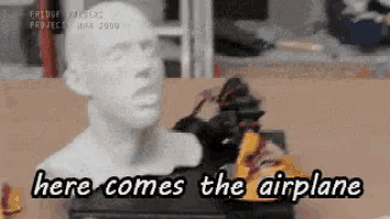 a statue of a man 's head with the words here comes the airplane below it